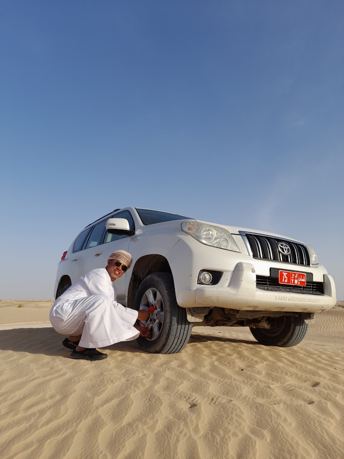 Muž v bílém obleku upouští pneumatiky u terénního auta v poušti Rub al khali