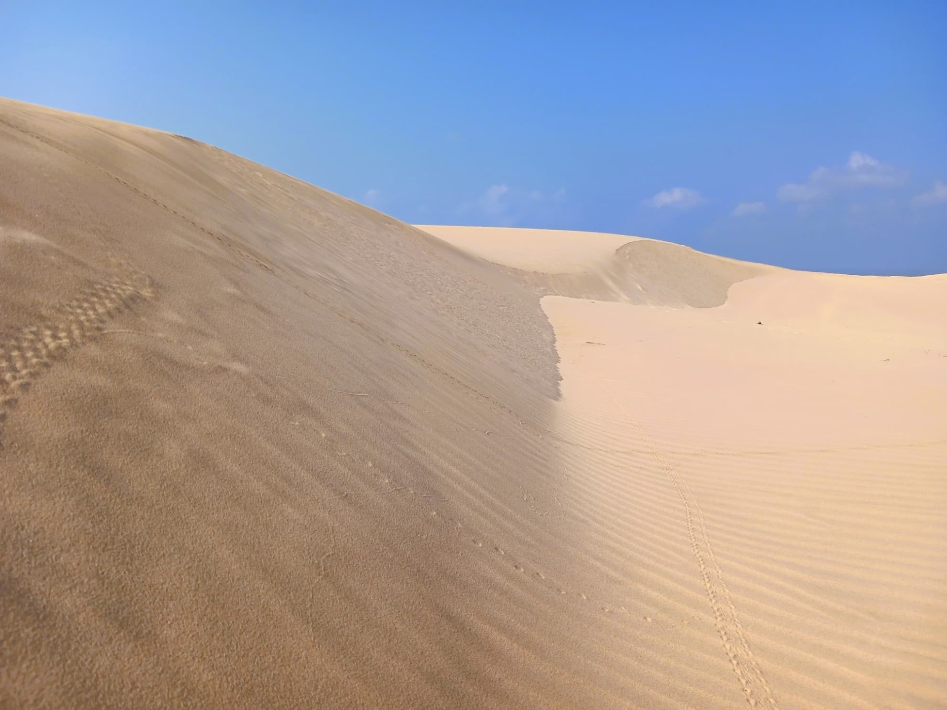 Obrázek zachycuje ikonické písečné duny u města Mirbat (Mirbat Sand Dunes), které leží v guvernorátu Dhofár v jižním Ománu.