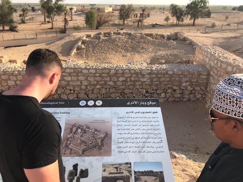 Dva návštěvníci stojí u informační tabule s archeologickým nalezištěm v Ubaru před pouští Rub al Khalí