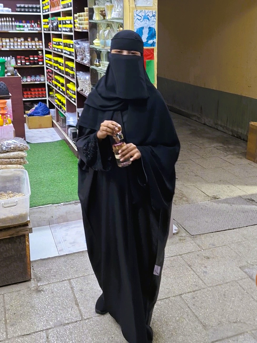 Žena v černém hidžábu na haffa souk v salalah nabízí parfém.
