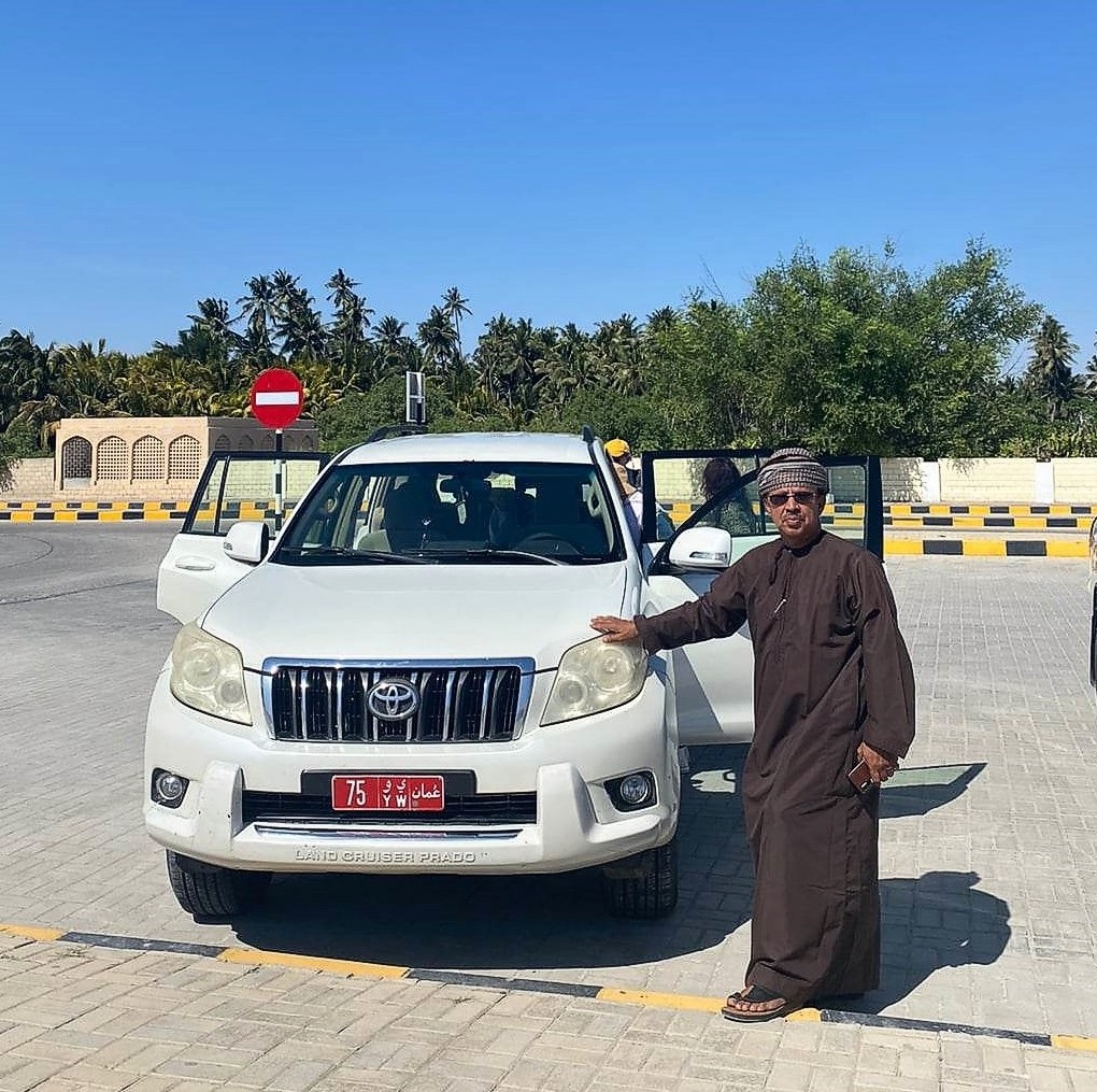 Muž stojí u bílé toyoty Land Cruiser na parkovišti muzea Země kadidla The Museum of the Frankincense Land, v Salalah v Ománu