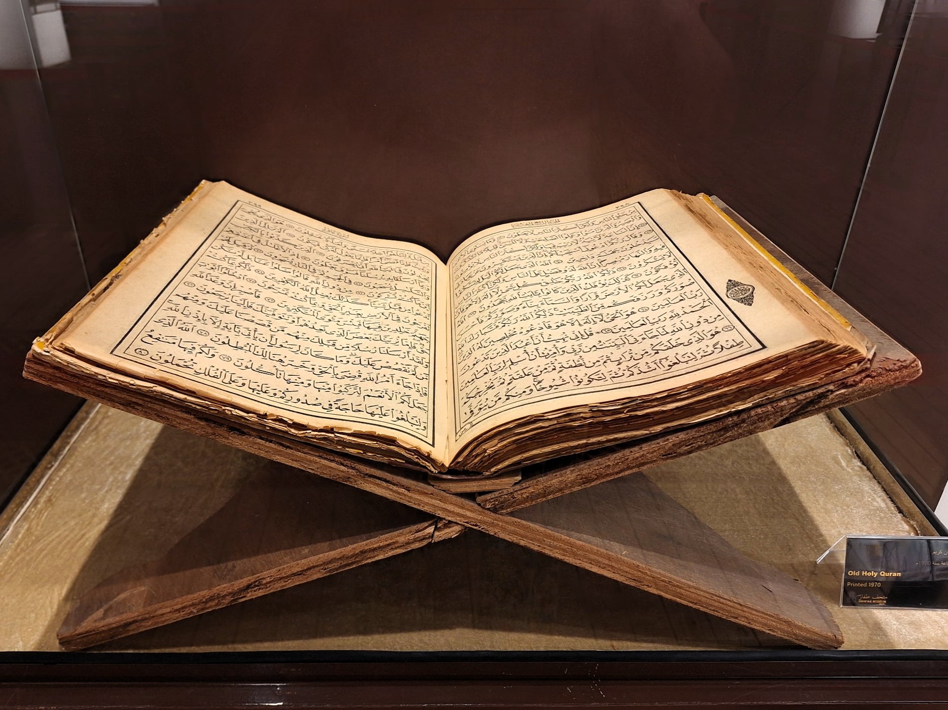Otevřená starý korán s arabským písmem leží v Salalah v muzeální vitríně na dřevěném stojanu.