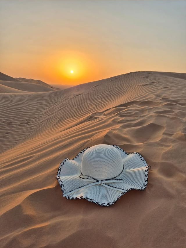 Bílý slaměný klobouk leží v písečných dunách Rub al Khali v Ománu při západu slunce