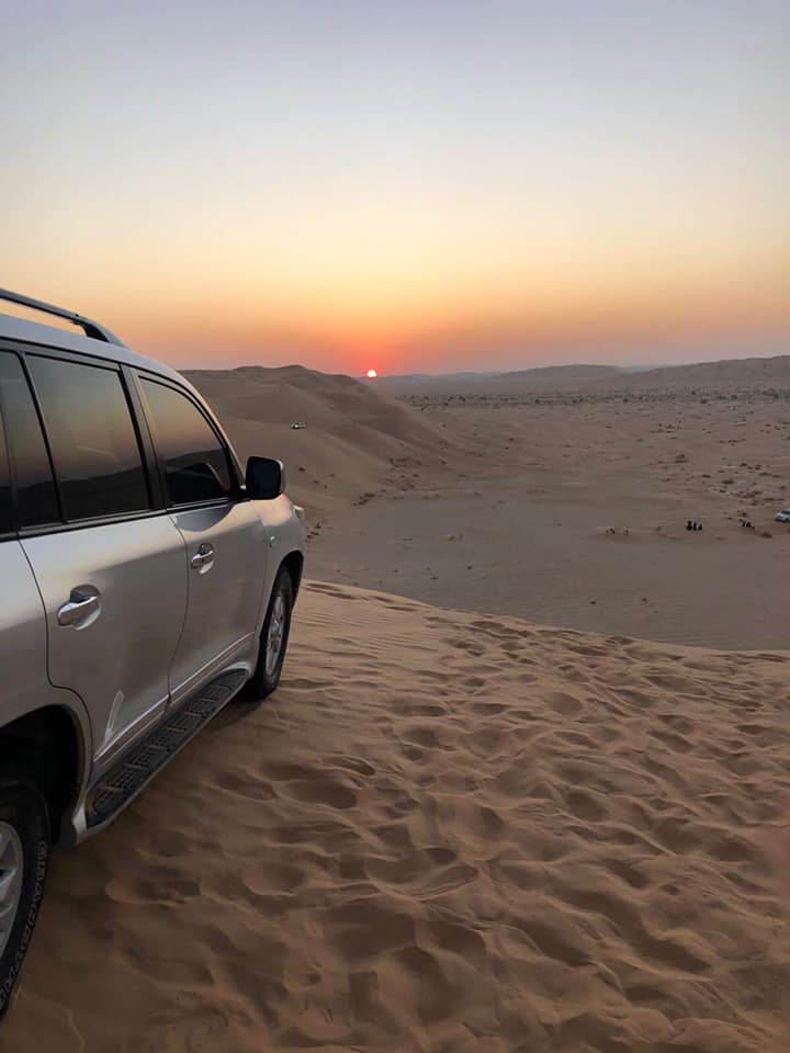 Bílý terénní vůz stojí v písečných dunách Rub al khali při západu slunce