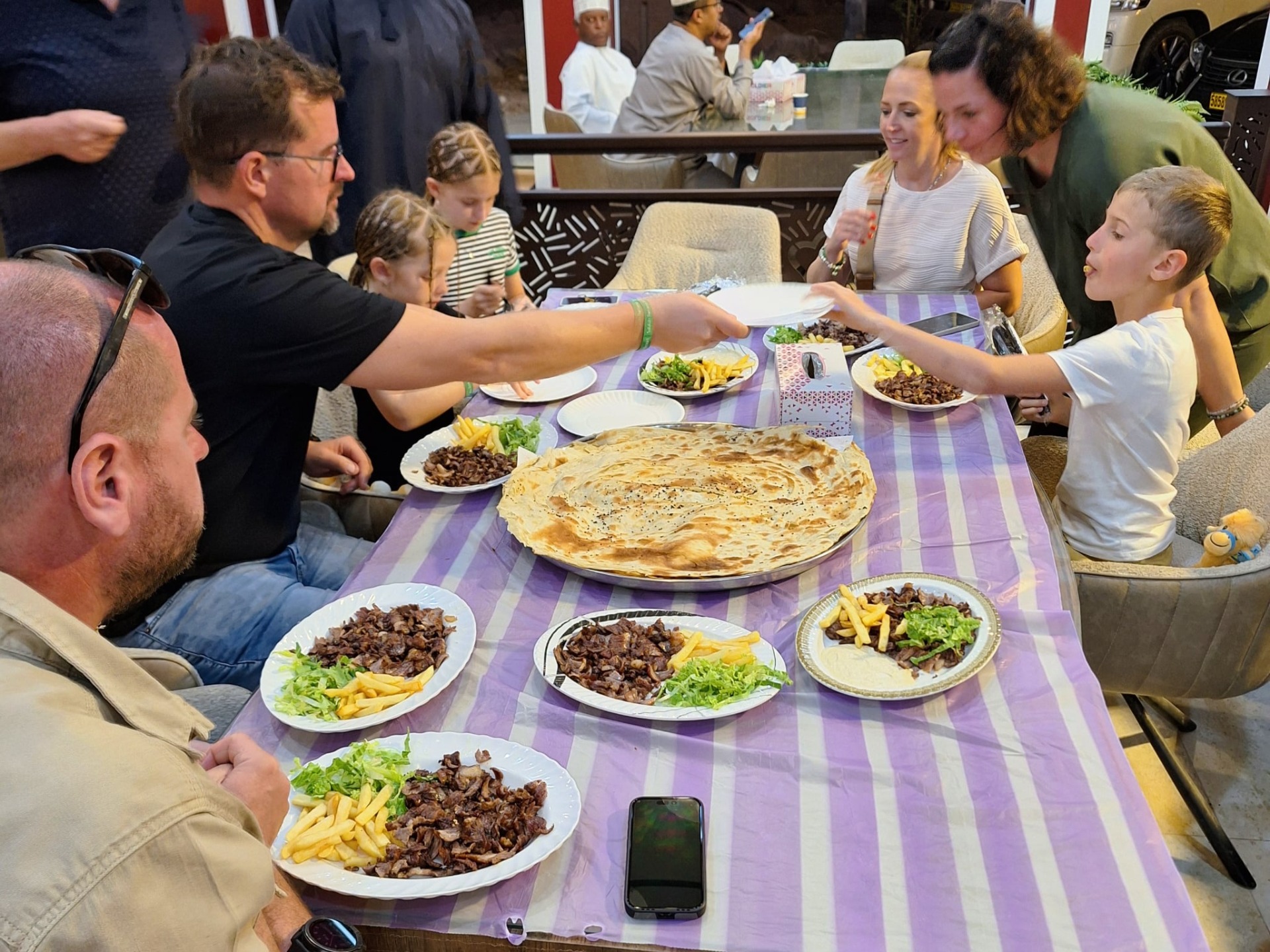 Rodina u stolu v restauraci v Salalah sdílí jídlo, děti i dospělí si podávají talíře s velbloudím masem.