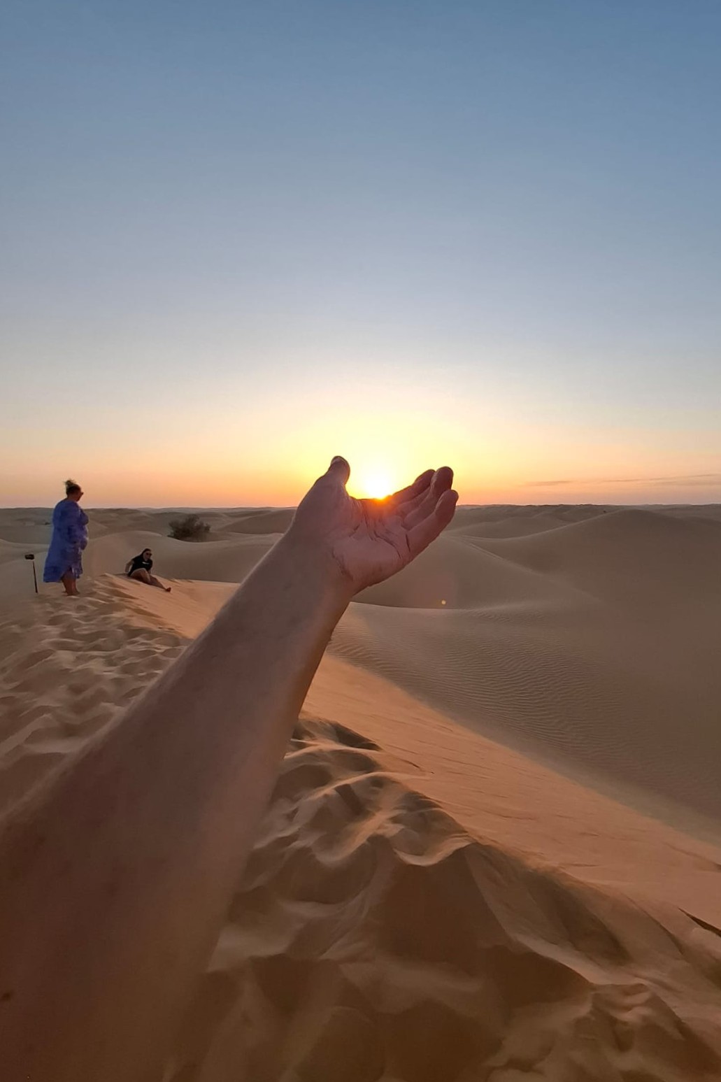 Západ slunce nad dunami v poušti Rub al khalí, ruka drží slunce v dlaních