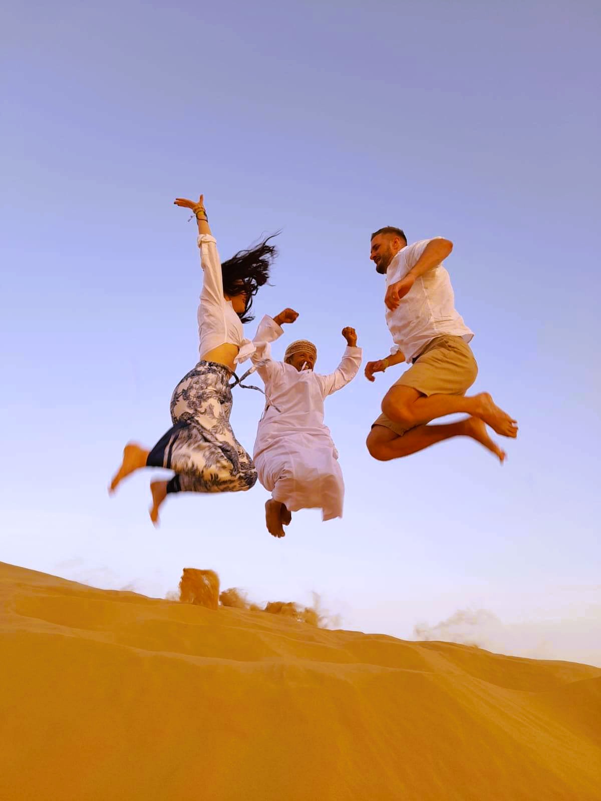 Tři lidé skáčou ve vzduchu nad dunami v poušti Rub al khali, zachycený pohyb a radost.