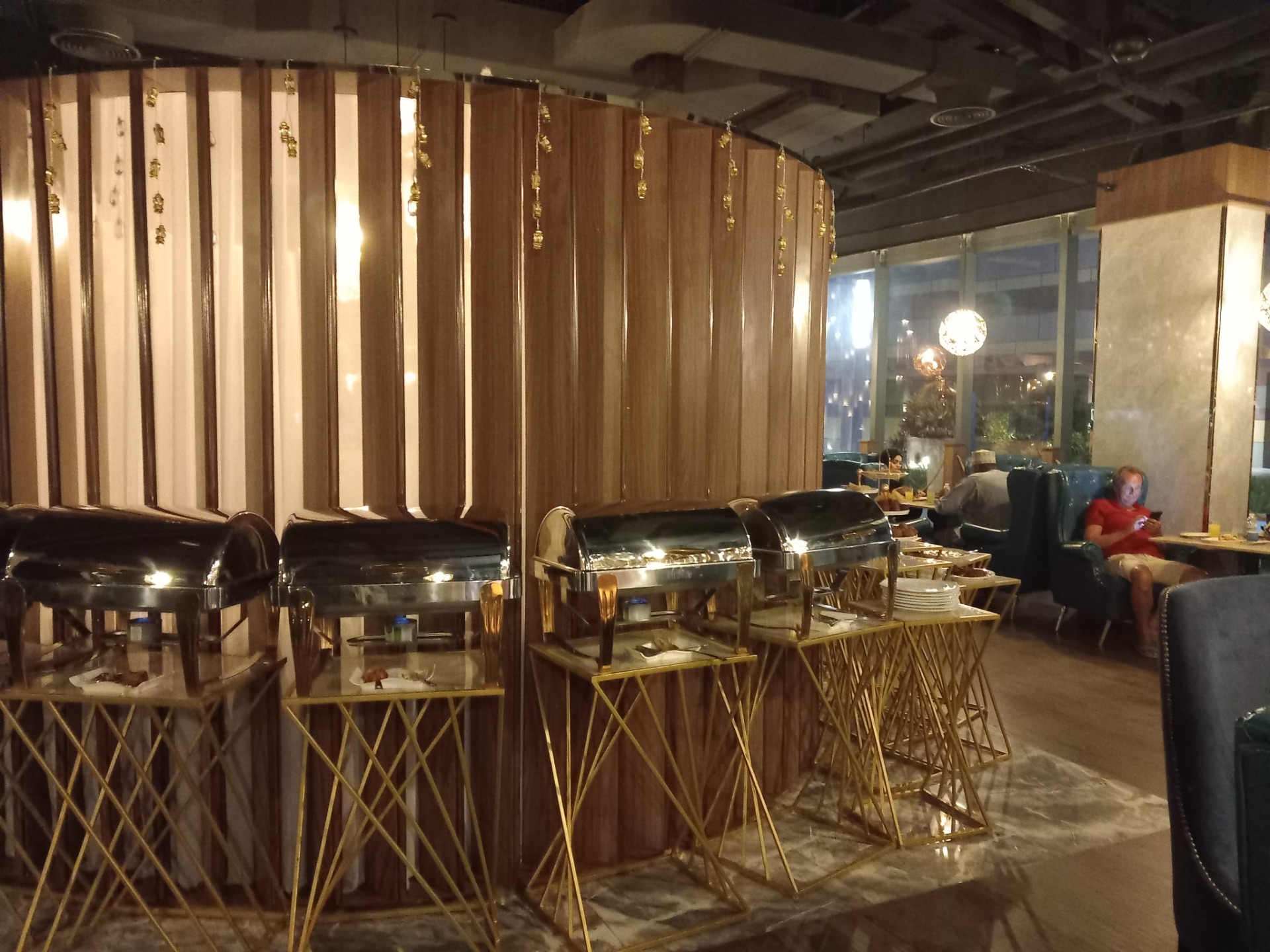 Interiér restaurace s bufetovými nerezovými ohřívači, zlatými stojany a dřevěnými příčkamiv nákupním centru Grand mall salalah