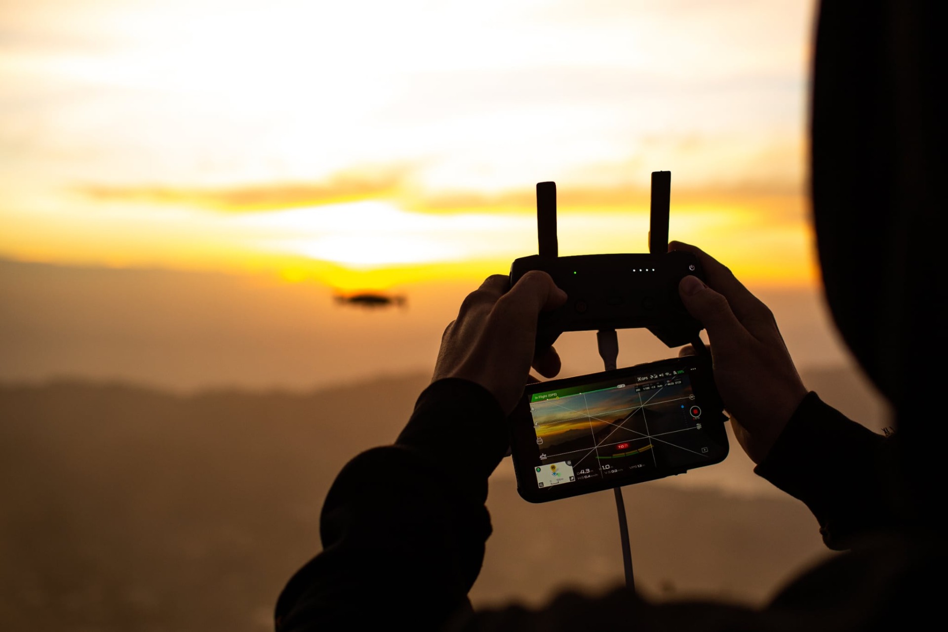 Silhoueta rukou drží dron s ovládacím tabletem při západu slunce nad dunami pouště Rub al khali v Ománu.