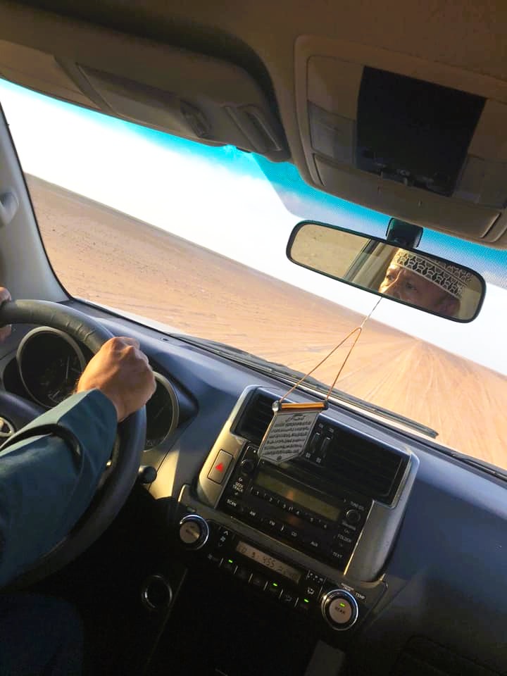 Řidič drží volant v autě, pohled na palubní desku a písečné duny Rub al Khalí přes čelní sklo.