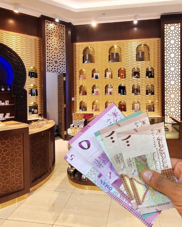 Ruka drží sadu ománských bankovek před prodejnou Arabian oud v Salalah